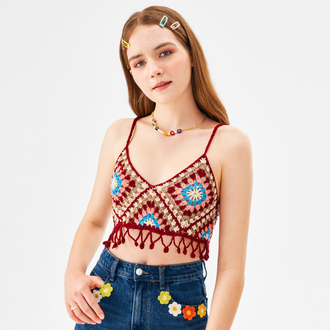 A young woman with long brown hair and colorful hair clips is wearing a crochet crop top and embellished jeans.