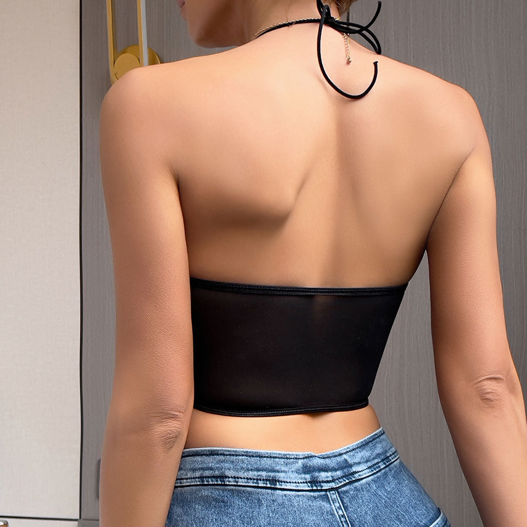 Back view of a woman wearing a black satin corset top with sheer mesh detailing at the back, paired with blue jeans.