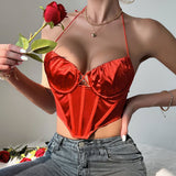 A woman wearing a red satin corset top with a halter neck and a rose in her hand.
