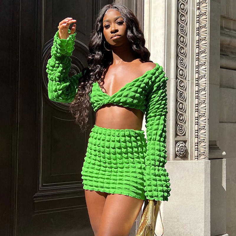 A Black woman poses in a vibrant green textured crop top and mini skirt set.
