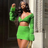 A Black woman poses in a vibrant green textured crop top and mini skirt set.