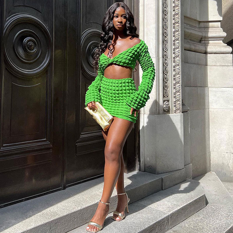 A woman in a green textured crop top and mini skirt stands on steps.