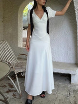 A woman poses in an outdoor alcove with a white dress and black ribbon shoulder details.