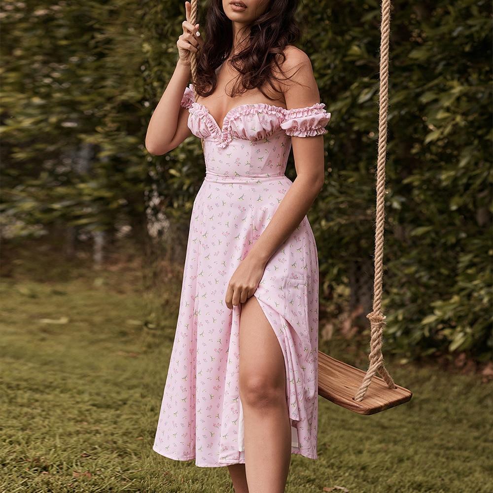 Woman wearing a pink floral off-the-shoulder midi dress with a high slit, standing next to a swing set outdoors.