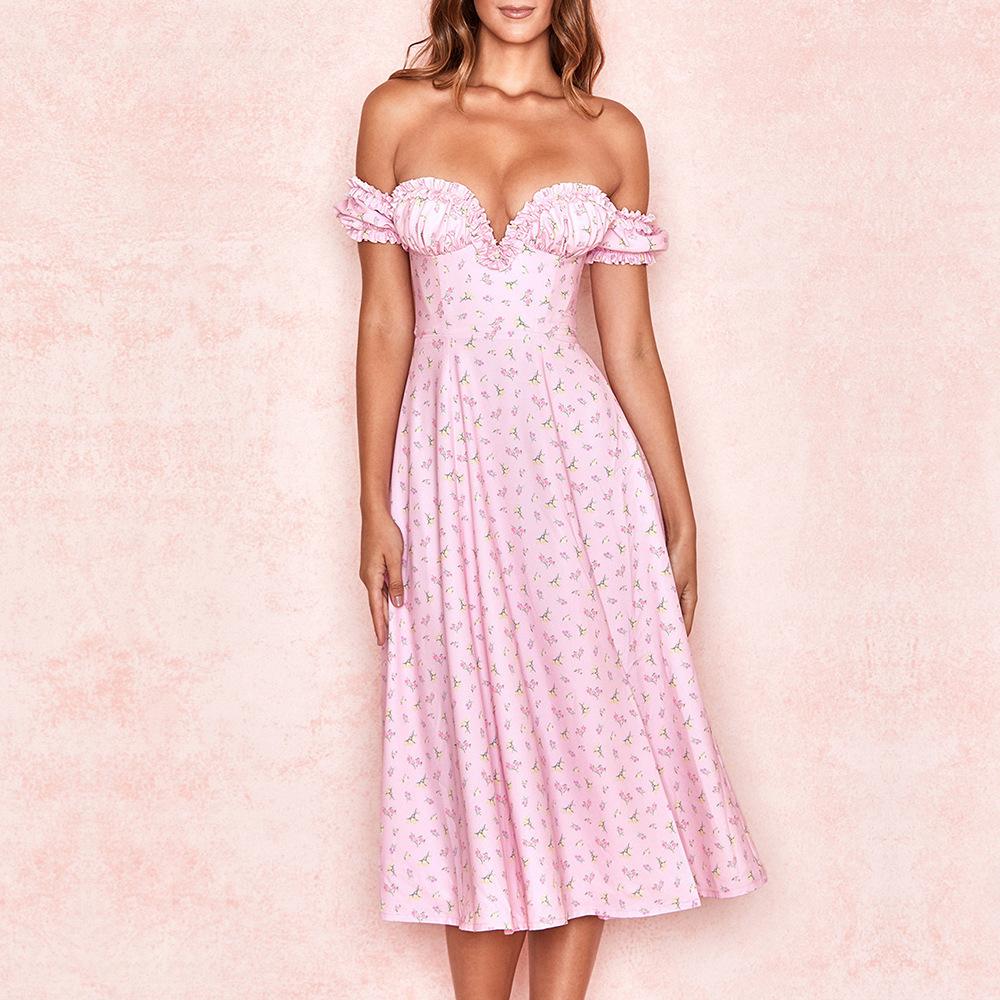 Woman wearing a pink floral off-the-shoulder midi dress with a sweetheart neckline and ruffled trim, standing against a pink background.