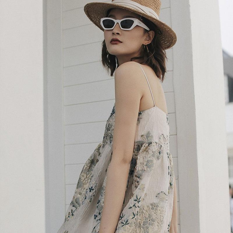 A woman in a floral dress, straw hat, and white sunglasses looking to the side.
