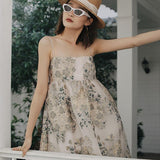 A woman in a floral dress and white sunglasses leaning on a railing.