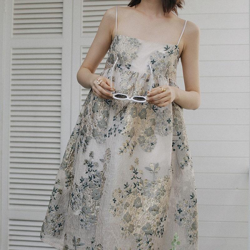 A woman in a floral dress holding white sunglasses.