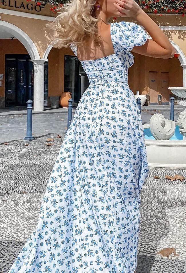 Woman in a white and blue floral print dress with puff sleeves, twirling in an outdoor plaza.