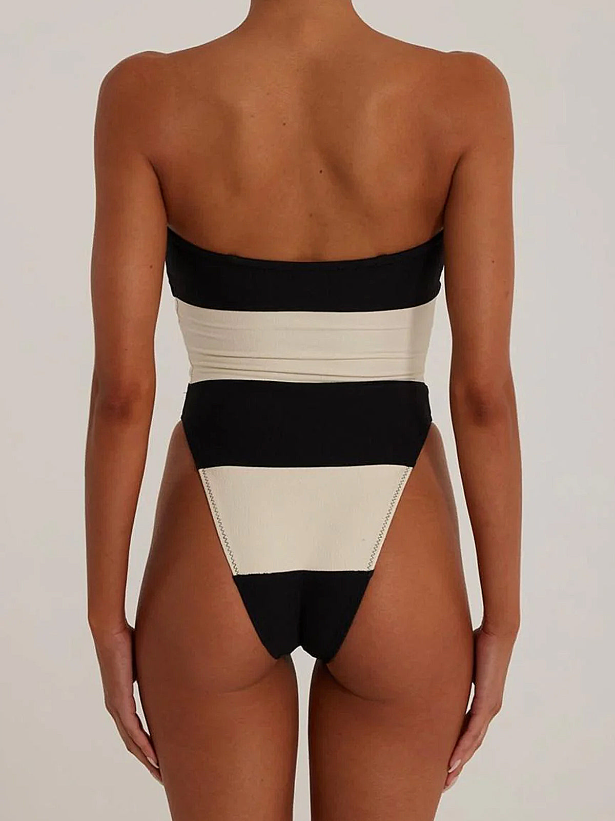 Back view of a woman wearing a black and white strapless one-piece swimsuit with high-cut legs and horizontal stripes.