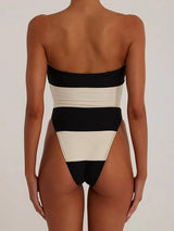Back view of a woman wearing a black and white strapless one-piece swimsuit with high-cut legs and horizontal stripes.