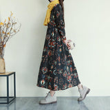 Woman wearing a black floral print midi dress with a yellow scarf and gray boots