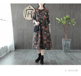 Woman wearing a black floral print midi dress with a black crossbody bag and black boots