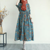 Woman wearing a teal floral print midi dress with an orange scarf and gray boots