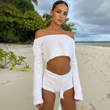 Woman in a white knit off-the-shoulder crop top and shorts on a beach