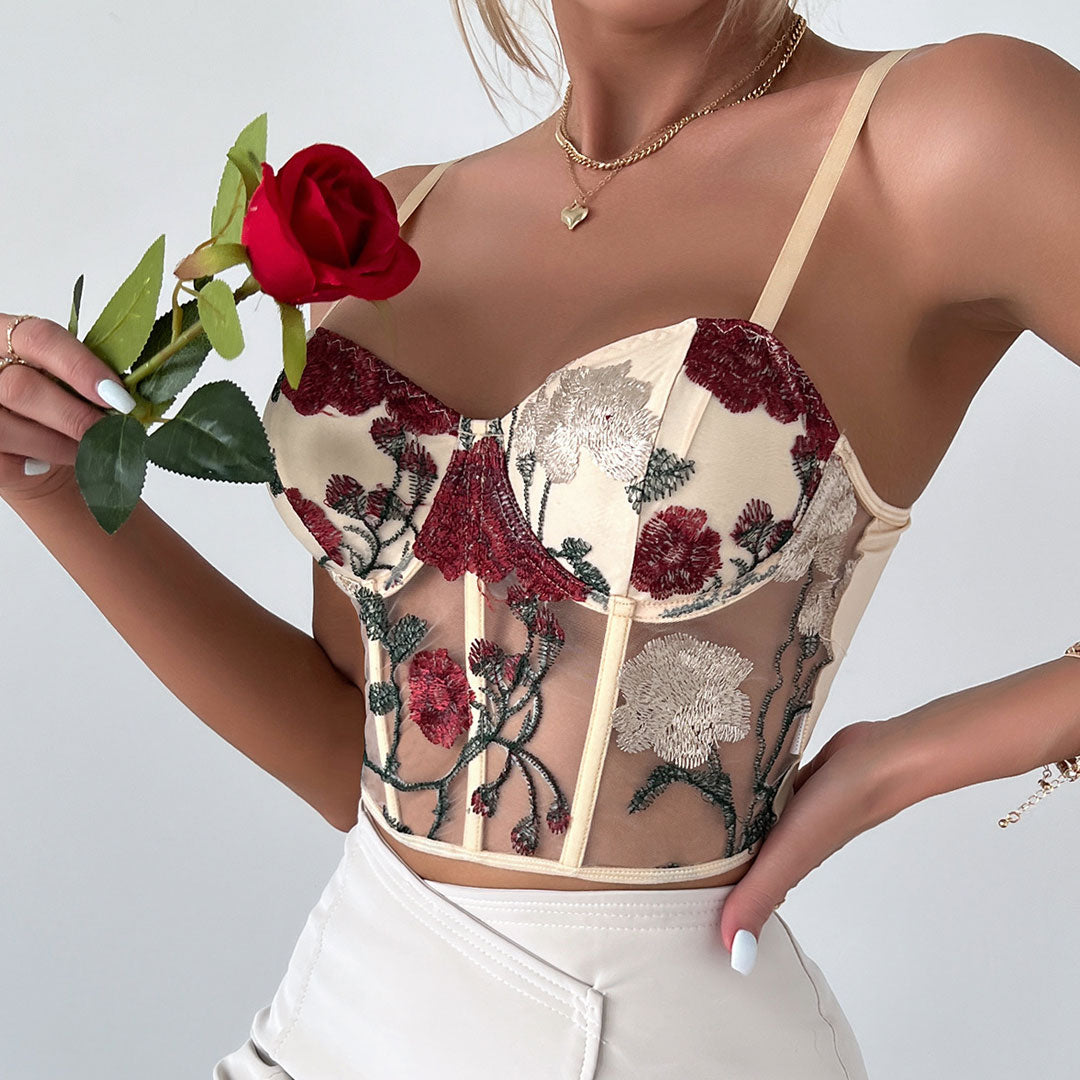 Woman wearing a cream corset top with red and white floral embroidery and a red rose