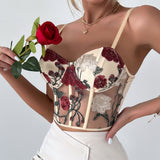 Woman wearing a cream corset top with red and white floral embroidery and a red rose