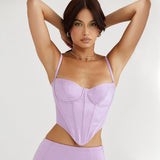 Close-up of a woman wearing a lavender corset top and mini skirt, looking at the camera with hands behind her head.