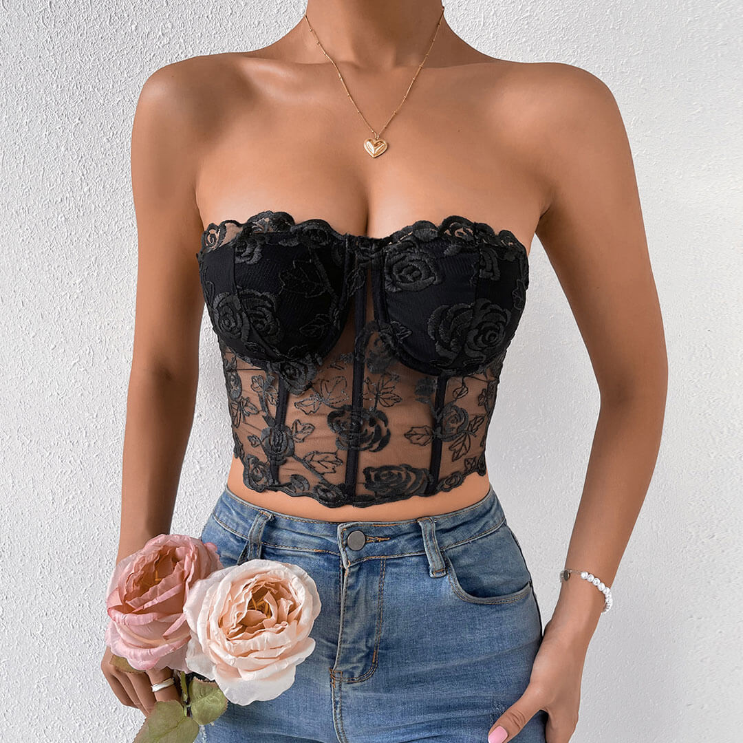 Woman wearing a black floral lace corset top with blue jeans and holding pink and peach roses.