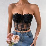 Woman wearing a black floral lace corset top with blue jeans and holding pink and peach roses.