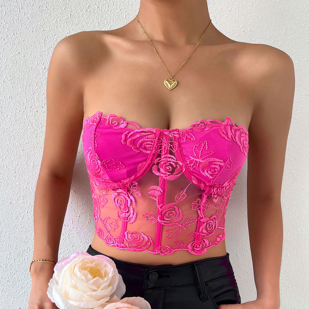 Woman wearing a pink lace corset top with floral embroidery and a gold heart necklace.