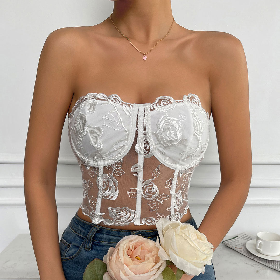 A woman wearing a white lace corset top with floral embroidery and a pink heart necklace.
