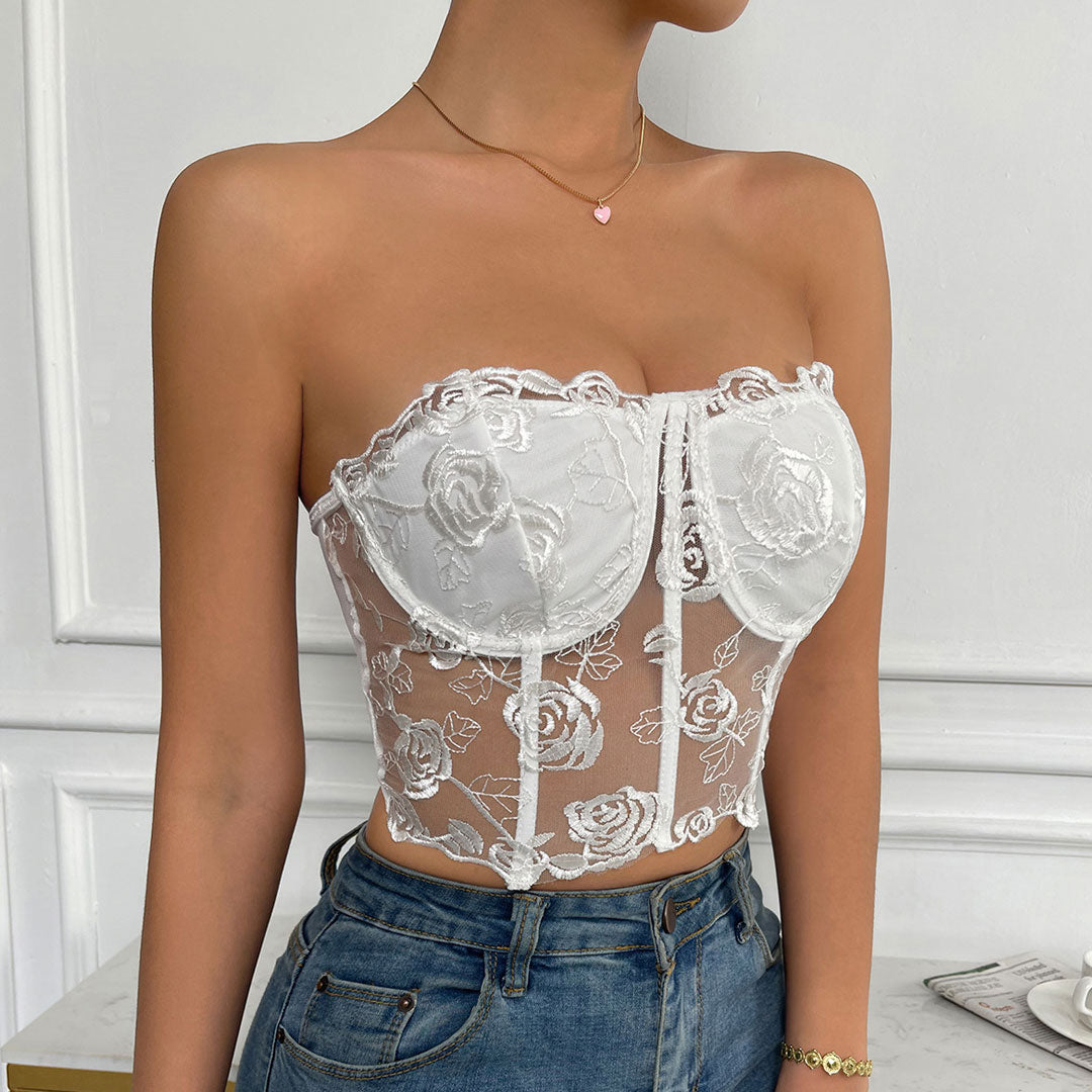A woman in a white lace corset top and blue jeans holding a bouquet of roses.