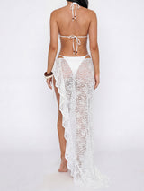 Back view of a woman wearing a white bikini and a sheer white lace sarong with a high slit and ruffled hem, against a white background.