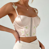 A woman wearing a beige satin corset top with butterfly embroidery and adjustable straps.