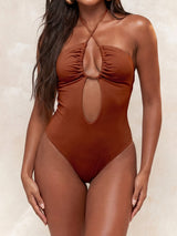 A woman wearing a brown one-piece swimsuit with a halter neck and a keyhole cutout.