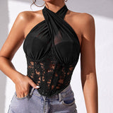 Close-up of a woman wearing a black halter neck lace and mesh corset top with blue jeans.
