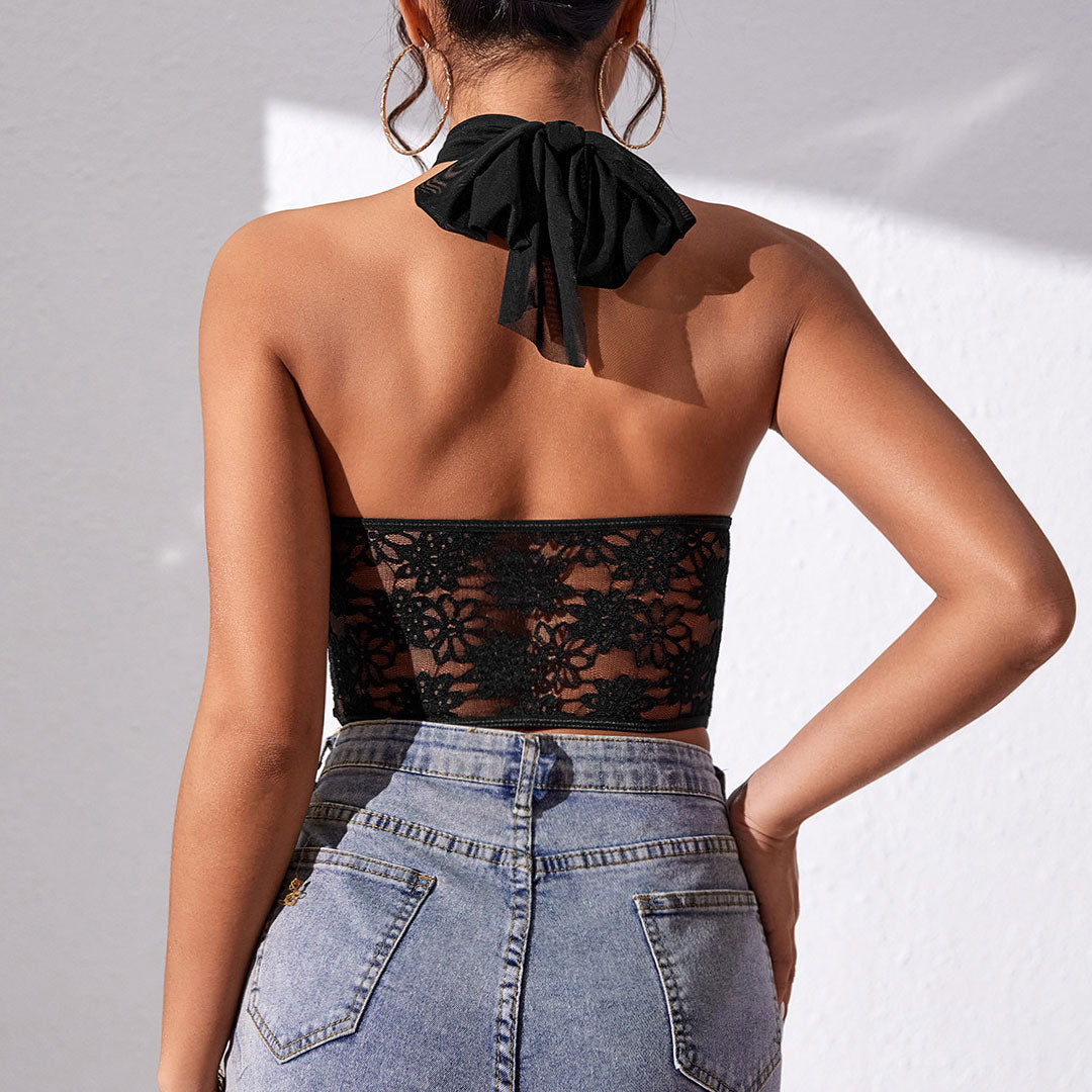 Back view of a woman wearing a black halter neck lace and mesh corset top with blue jeans.