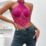 A woman wearing a pink halter top with lace detailing and blue jeans, standing in front of a white wall.