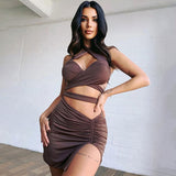 Woman wearing a brown halter neck two-piece dress with a ruched skirt and thigh-high slit, standing in front of a white brick wall.