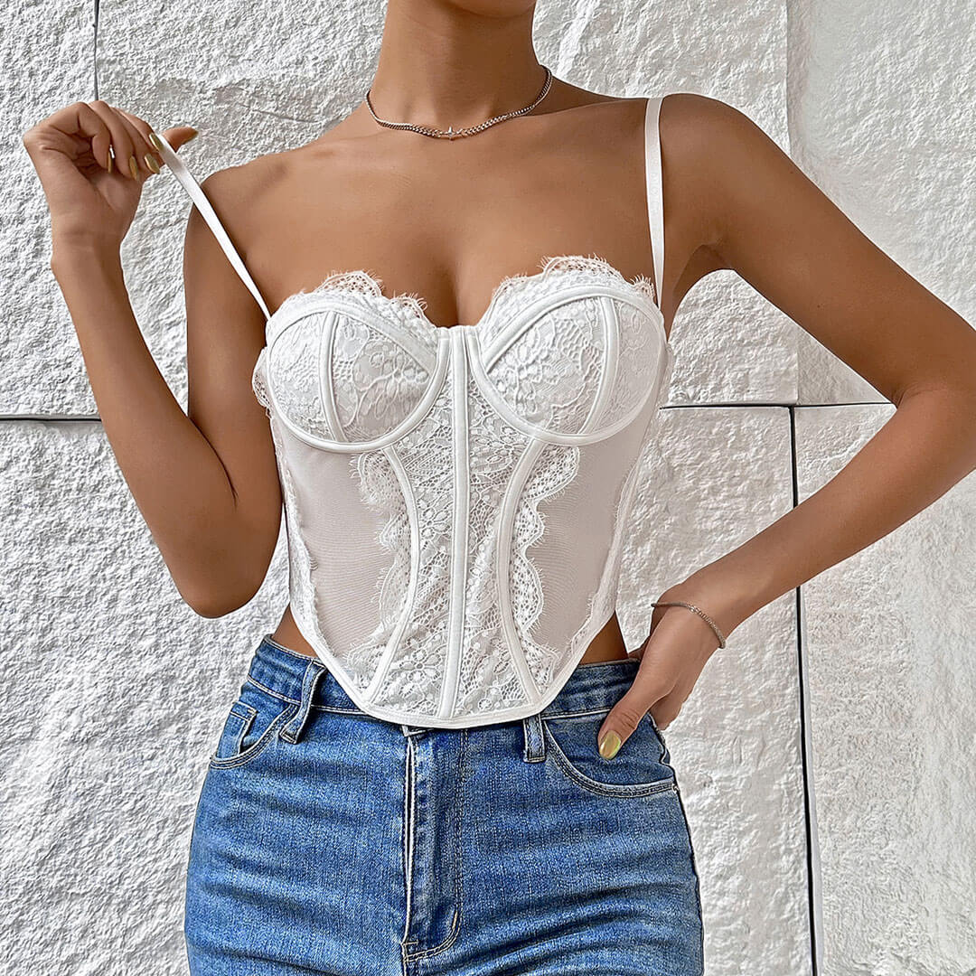 A woman wearing a white lace corset top and blue jeans, with her hand on her hip.