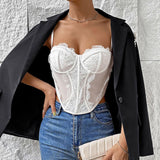 A woman wearing a white lace corset top and blue jeans, with a black blazer draped over her shoulders.