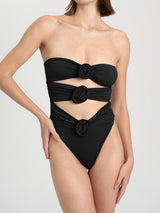 Front view of a woman wearing a black strapless one-piece swimsuit with cut-out details and floral appliques.