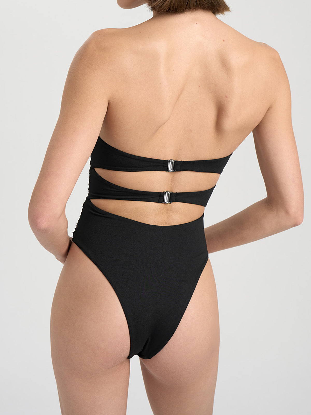 Side view of a woman wearing a black strapless one-piece swimsuit with cut-out details and floral appliques.