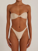 A woman wearing a beige strapless bikini with a knotted bust and high-cut bottoms, front view.