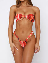 Woman wearing a red and orange tie-dye strapless bikini with a tie-front top and high-cut bottoms.