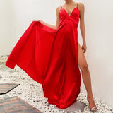 Woman in a red satin dress with a high slit and spaghetti straps, lifting the skirt