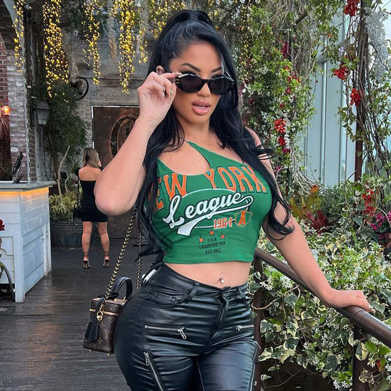Woman adjusting her sunglasses while wearing a green New York graphic print crop top and black leather pants