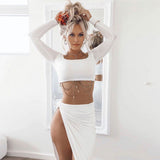 Woman in a white long-sleeved crop top and a white high-slit skirt, posing in front of a mirror.
