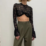 woman wearing a black lace crop top with bell sleeves and olive green high-waisted pants