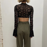back view of a woman wearing a black lace crop top with bell sleeves and olive green high-waisted pants