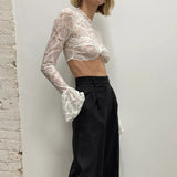 side view of a woman in a white lace crop top and black pants