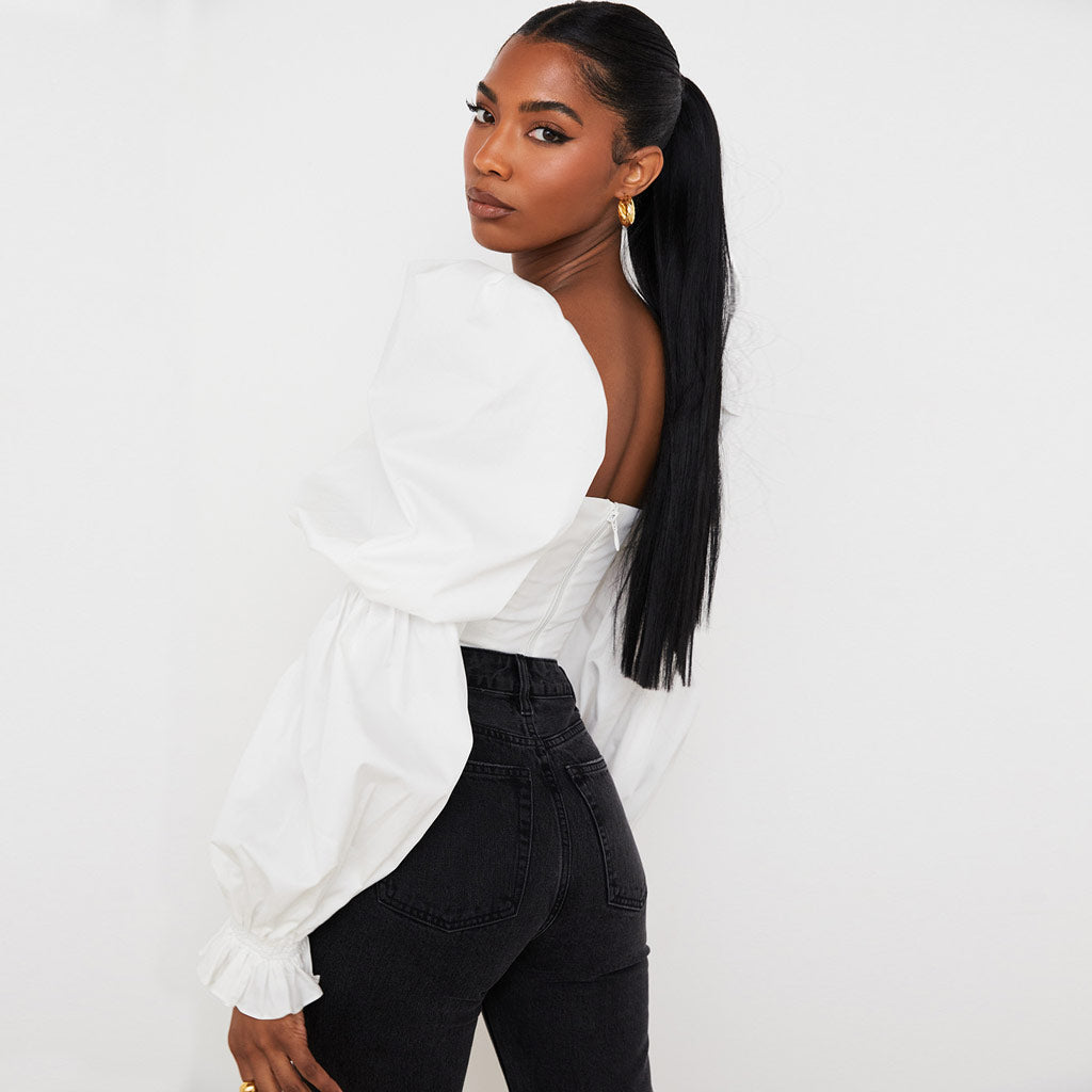 Woman wearing a white off-the-shoulder crop top with puff sleeves and black jeans, viewed from the back.