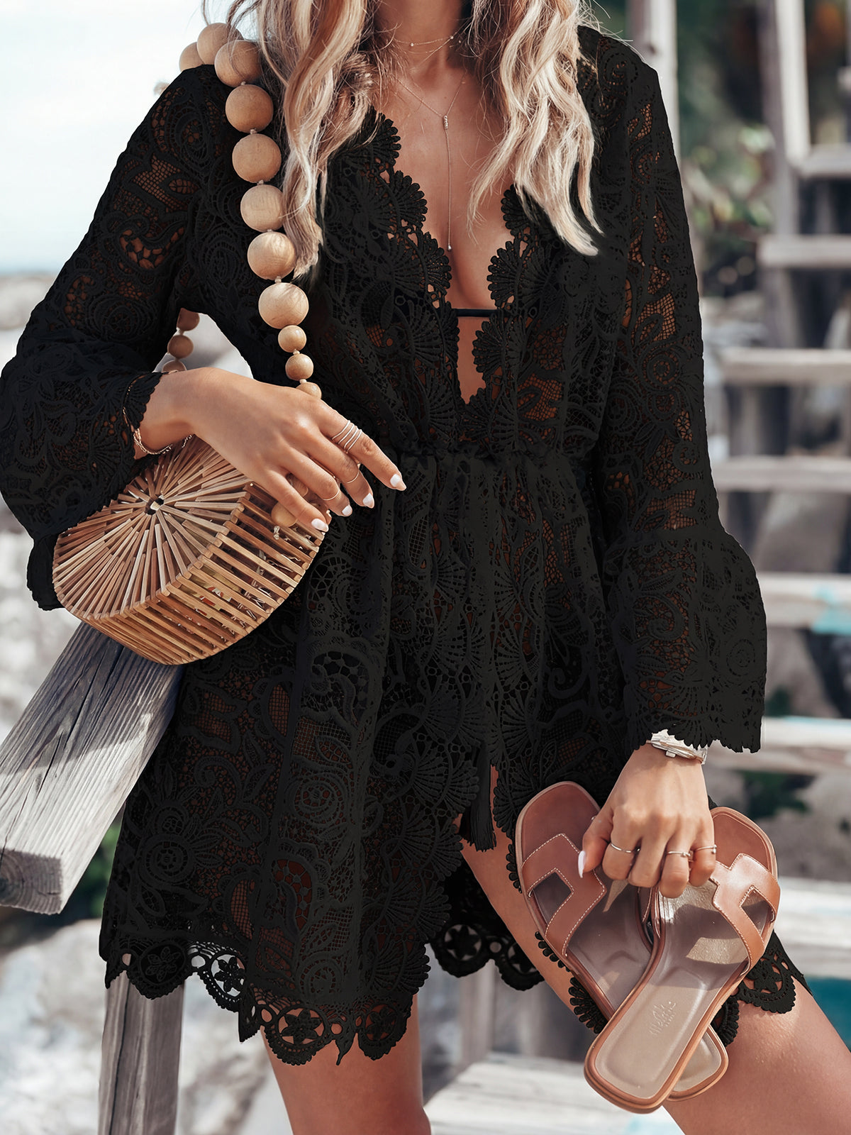 Woman wearing a black lace cover-up with a straw bag and sandals