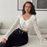 Woman sitting on a couch wearing a white lace crop top with long sleeves and black pants