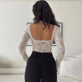 Back view of a woman wearing a white lace crop top with long sleeves and black pants